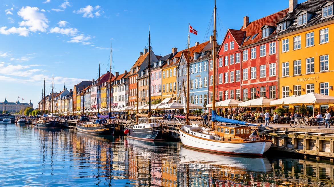 Colourful historic buildings, sailing boats and waterfront cafés along Nyhavn Canal in Copenhagen, Denmark.